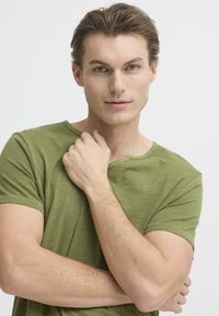 Oliwkowa, krótka koszulka z okrągłym dekoltem. Miękka w dotyku, luźny krój, z widocznymi przeszyciami na rękawach i dole.