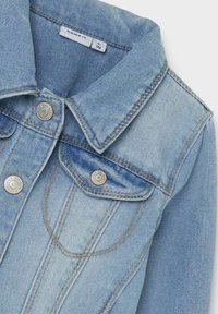 Ljusblå denimjacka med klassisk krage, silverfärgade knappar och bröstfickor med detaljerad stickning.