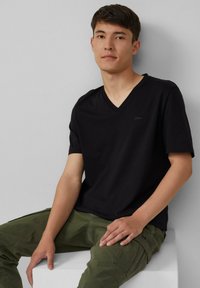 Zwarte korte mouwen V-hals t-shirt van gladde stof, gecombineerd met olijfgroene cargobroek met zakken en stiksels.