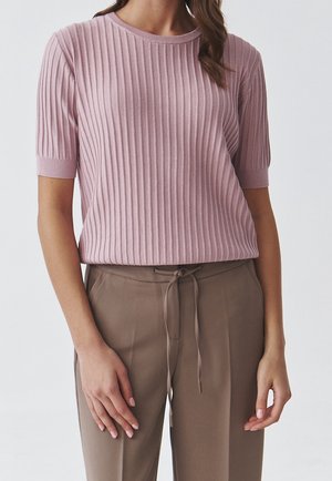 Woman wearing a ribbed, short-sleeve mauve sweater and high-waisted taupe pants tied with a front drawstring, standing with hands relaxed.