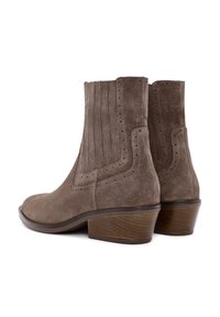 Botas de ante marrón hasta el tobillo con bajos tacones de madera apilados y detalles de perforación decorativa a lo largo de los lados y la parte trasera.