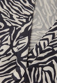 Tessuto blu navy e crema con motivi a strisce astratte simili a zebre. Presenta un design a collo a V e dettagli di cucitura visibili. Texture morbida.