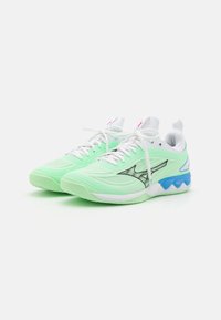 Scarpe da ginnastica verde chiaro con tessuto in rete, lacci bianchi, logo nero e accenti blu sulla suola; design aerodinamico e superficie testurizzata.