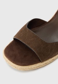 Brown suede espadrille wedge sandal featuring a wide strap and woven jute sole. Smooth inner lining with contrasting dark accents.