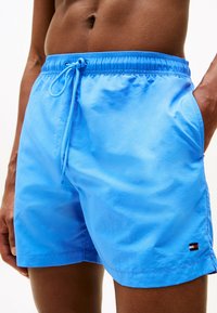 Costumi da bagno blu brillante con vita elastica e cordino. Presentano tasche laterali e una piccola etichetta con logo in rosso, bianco e nero.