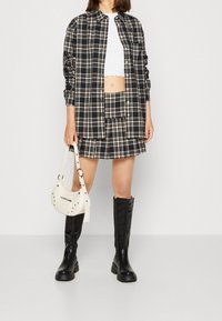 Camicia oversize a scacchi bianco e nero, top corto bianco, gonna a scacchi abbinata, stivali neri al ginocchio e una borsa color crema con dettagli in borchie.