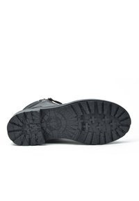 Calzado negro con una suela de goma texturizada que presenta surcos profundos para un mejor agarre, costuras reforzadas y una parte superior lisa con un detalle de cremallera.