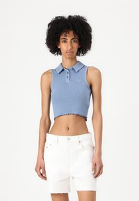 Lyseblå, kort ribbet polo med krage og tre knapper, med rå kant. Kombinert med hvite denimshortser.