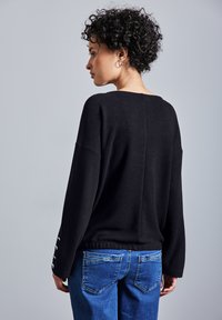 Maglione nero in lavorazione a maglia con una vestibilità rilassata, spalle scese e texture a costine. Abbinato a jeans in denim blu con tasche posteriori.