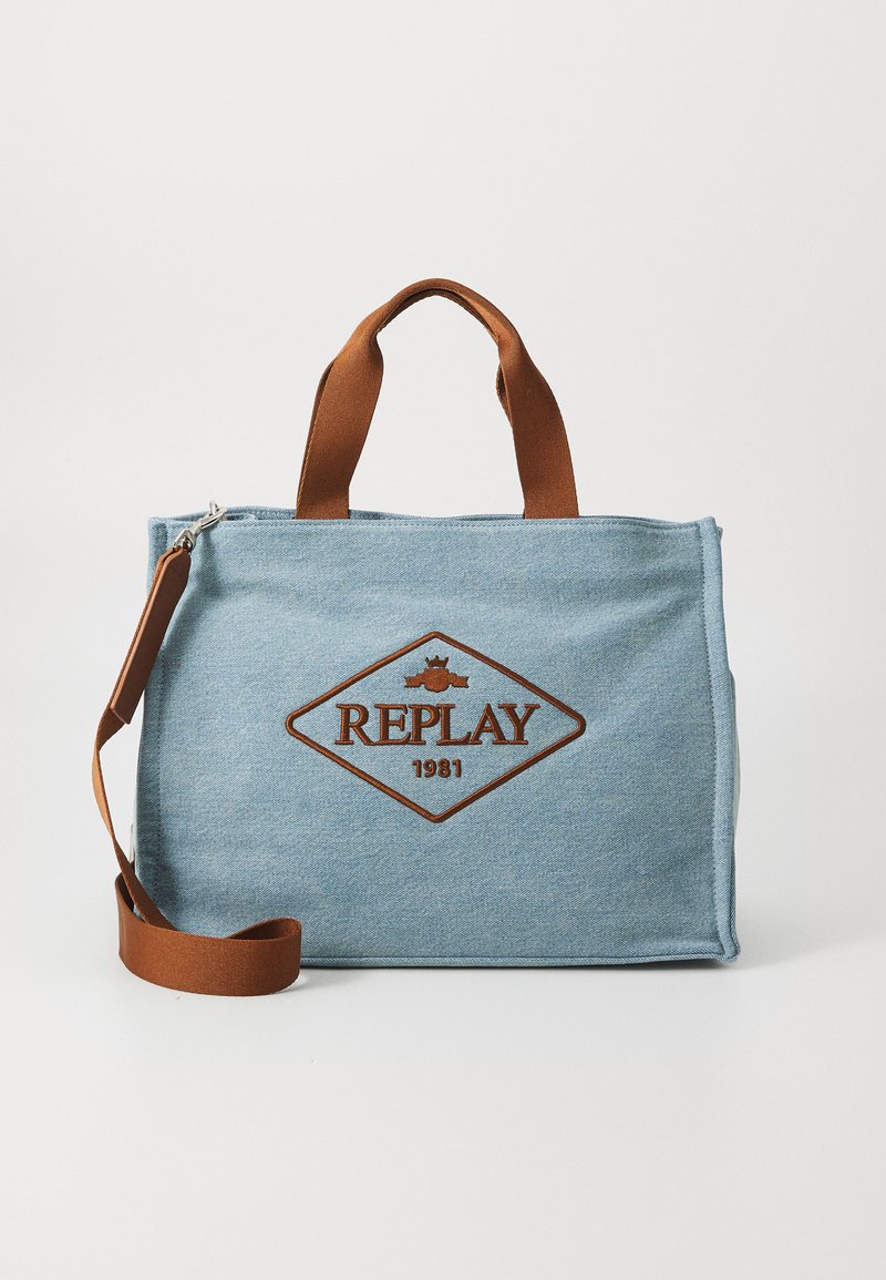 Blue denim tote bag with brown fabric handles and an adjustable shoulder strap. Features a diamond logo patch with "REPLAY" and "1981."