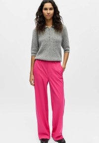 Pull gris à manches courtes avec col et boutons, associé à un pantalon large rose vif. Texture lisse et coupe ajustée.