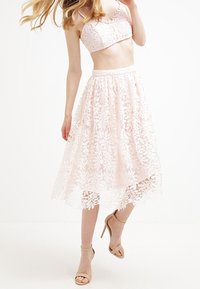 Conjunto de dos piezas de encaje que incluye un top corto rosa y una falda a la altura de la rodilla con patrones florales, combinado con sandalias de tacón nude.