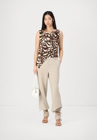 Top senza maniche marrone e bianco a fantasia abbinato a pantaloni beige a vita alta e sandali beige con cinturino. Comprende una piccola borsa bianca.