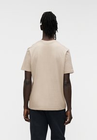 Μπεζ βαμβακερό T-shirt με κοντά μανίκια και στρογγυλή λαιμόκοψη, εμφανιζόμενο από πίσω. Ομαλή υφή, άνετη εφαρμογή, χωρίς ορατά λογότυπα ή σχέδια.