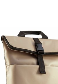 Beige waterdichte tas met een opgevouwen klep, zwarte ritssluiting en sluiting met een band. Bevat een handvat aan de bovenkant en een voorvak voor gemakkelijke toegang.