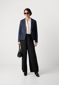 Denim blazer med spiss lapel, mørk vask, hvit plisserte bluse, vide svarte bukser, svart håndveske og solbriller. Glatte teksturer, skreddersydd passform.