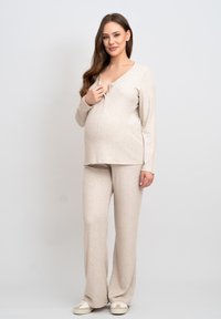 Beige amningsset i lounge-stil med en långärmad topp med djup V-ringning och knäppning, tillsammans med vida byxor i ett mjukt, texturerat tyg.