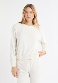 Bluza w kolorze kremowym z okrągłym dekoltem, długimi rękawami i prążkowanym obszyciem. Całość zdobi delikatny wzór gwiazdek. Miękka tekstura materiału.