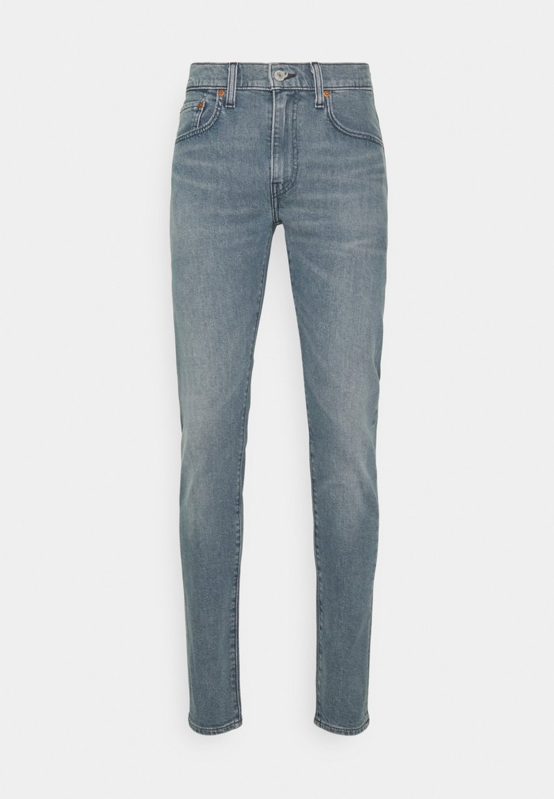 Jeans de mezclilla desgastados de color azul, con un corte ajustado, diseño de cinco bolsillos y detalles de costura sutiles cerca de la cinturilla y los bolsillos.