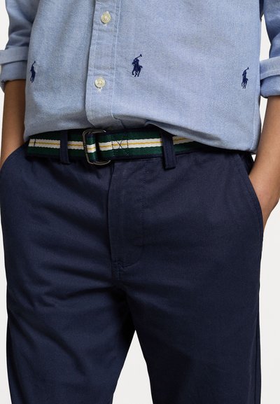 Camicia azzurra chiara con piccoli loghi di cavallo blu scuro, abbinata a pantaloni blu navy e una cintura intrecciata a strisce verdi.