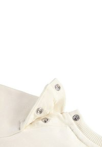 Un capo di abbigliamento color crema con una texture a maglia, dotato di bottoni a pressione al colletto e dettagli a coste lungo i bordi.