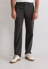 Ciemnoszare bawełniane spodnie o prostym kroju nogawek, z zapięciem na guziki z przodu i tylnymi kieszeniami. Noszone z białymi trampkami.