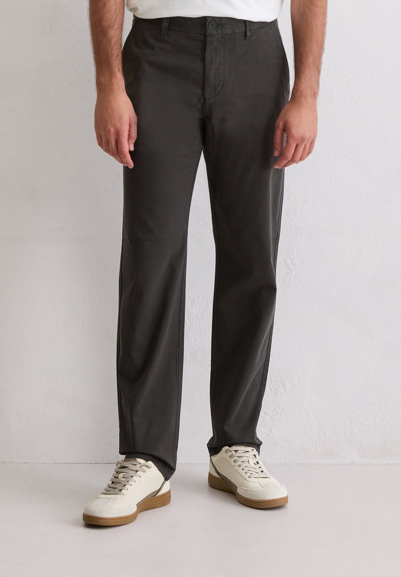 Ciemnoszare bawełniane spodnie o prostym kroju nogawek, z zapięciem na guziki z przodu i tylnymi kieszeniami. Noszone z białymi trampkami.