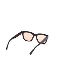 Ochelari de soare supradimensionați, de culoare neagră, cu formă de ochi de pisică și lentile roz. Ramele sunt lucioase, cu margini plate și branding subtil pe tâmple.
