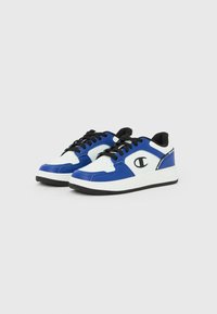 Χαμηλά αθλητικά παπούτσια σε λευκό και μπλε με μαύρα κορδόνια, μαύρη εσωτερική επένδυση και μαύρο λογότυπο στο πλάι, απεικονισμένα σε λευκό φόντο.