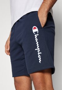 Pantalones cortos de algodón azul marino con cintura elástica. Presenta el logo bordado en blanco de "Champion" en el costado y un acento de marca encima del logo.