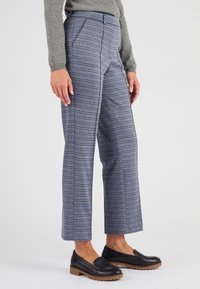 Maglione grigio, pantaloni a quadri in tonalità blu e marrone, con taglio dritto, tasche laterali e scarpe nere piatte con suola in legno.