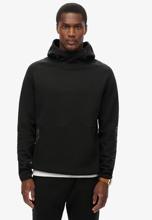 Sweat-shirt noir avec un col haut, des cordons de serrage, des poignets côtelés et une poche frontale. Présente un logo texturé sur la poitrine et des accents sur les manches.