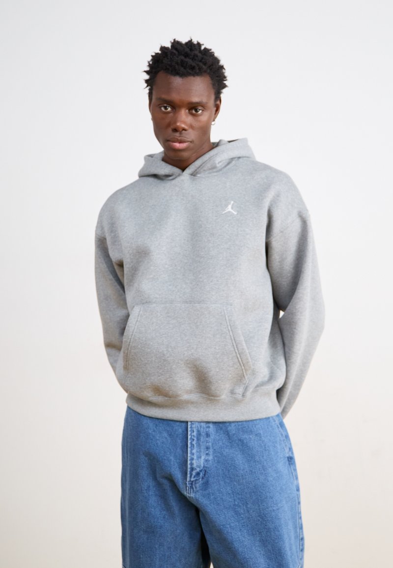 Sweat-shirt à capuche gris avec poche kangourou et logo blanc ; associé à un jean en denim bleu. Texture douce, coupe décontractée.
