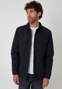 Donkerblauwe knoopsluiting shirt van katoen, met twee borstzakken, een corduroy kraag en een ontspannen pasvorm, gedragen over een wit T-shirt.