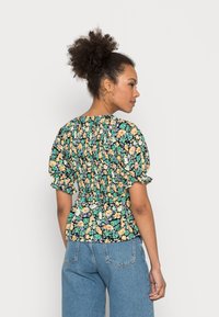 Blusa floral com fundo escuro, com costas franzidas e mangas curtas com volume. Apresenta flores coloridas e um ajuste descontraído. Combinada com jeans azuis.