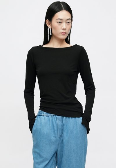 Top preto de mangas compridas com decote barco, textura suave, design ajustado, combinado com calças de ganga azuis claras e casuais.