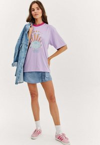 Fialové př oversized triko s grafickým potiskem, světle modrá džínová sukně a růžové tenisky. Měkčená textura, uvolněný střih a vrstvený vzhled.