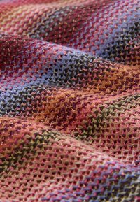 Gros plan d'un tissu tricoté texturé avec des motifs ondulés dans des tons de violet, rose, orange et vert.