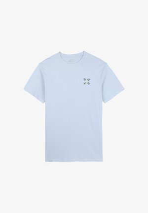 T-shirt en coton bleu clair à manches courtes et col rond, arborant un petit motif floral vert et jaune sur le côté gauche de la poitrine.