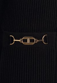 Tessuto nero a coste con una fibbia metallica dorata che presenta una forma ovale e un design intrecciato, fissata da anelli di tessuto nero.