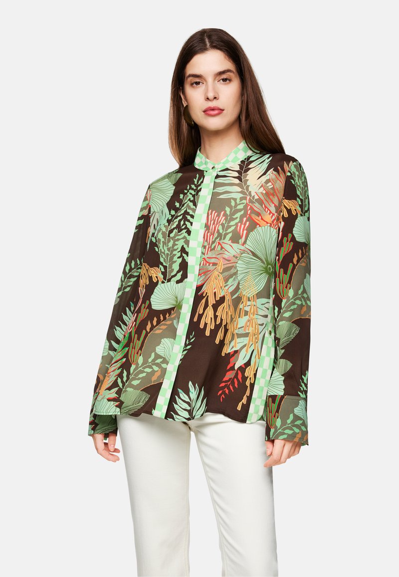 Brown shirt featuring a green leafy print, long sleeves, a collar, and a green checkered button placket. White pants complete the outfit.
