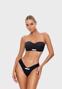 Černý bikini set s nevystuženým topem hladké textury a vysokými kalhotkami s V-výřezem. Štítek na obou kusech.