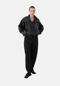 Chaqueta oversized de cuero negro con cuello alto, combinada con pantalones negros holgados. Diseño sencillo, textura suave, sin patrones visibles.