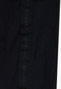 Pantaloni sportivi neri realizzati in tessuto testurizzato con una prominente fascia nera con il logo "JORDAN" lungo il lato per un tocco di branding.