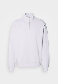 Pull-over blanc à manches longues avec col montant et demi-fermeture éclair à l'avant, poignets et ourlet côtelés.