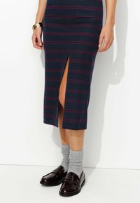 Jupe crayon en tricot bleu marine avec des rayures bordeaux, dotée d'une fente sur le côté. Associée à des chaussettes grises et des mocassins marron foncé.