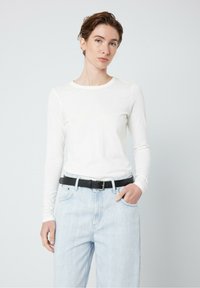 Långärmad vit topp i lätt tyg med rundad halsringning. Matchas med ljusblå högmidjade jeans och ett svart bälte.