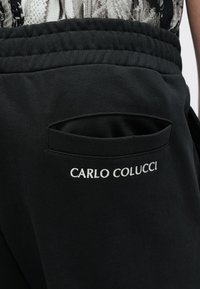 Schwarze Jogginghose mit elastischem Bund, einer Seitentasche und dem in Weiß gestickten Namen "CARLO COLUCCI". Weiche Stofftextur.