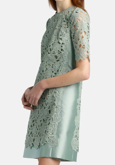 Mintgroene jurk met een kanten overlay met bloemvormige patronen, korte mouwen en een glanzende satijnen afwerking. Elegante ontwerpen met een getailleerde silhouet.