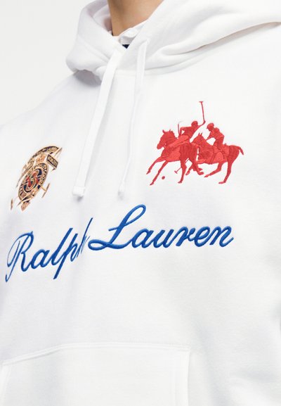Λευκό φούτερ με κουκούλα με μπλε γραφικά "Ralph Lauren", κόκκινες κεντημένες φιγούρες παίκτων πόλο σε άλογα και χρυσό κεντημένο έμβλημα στο στήθος.